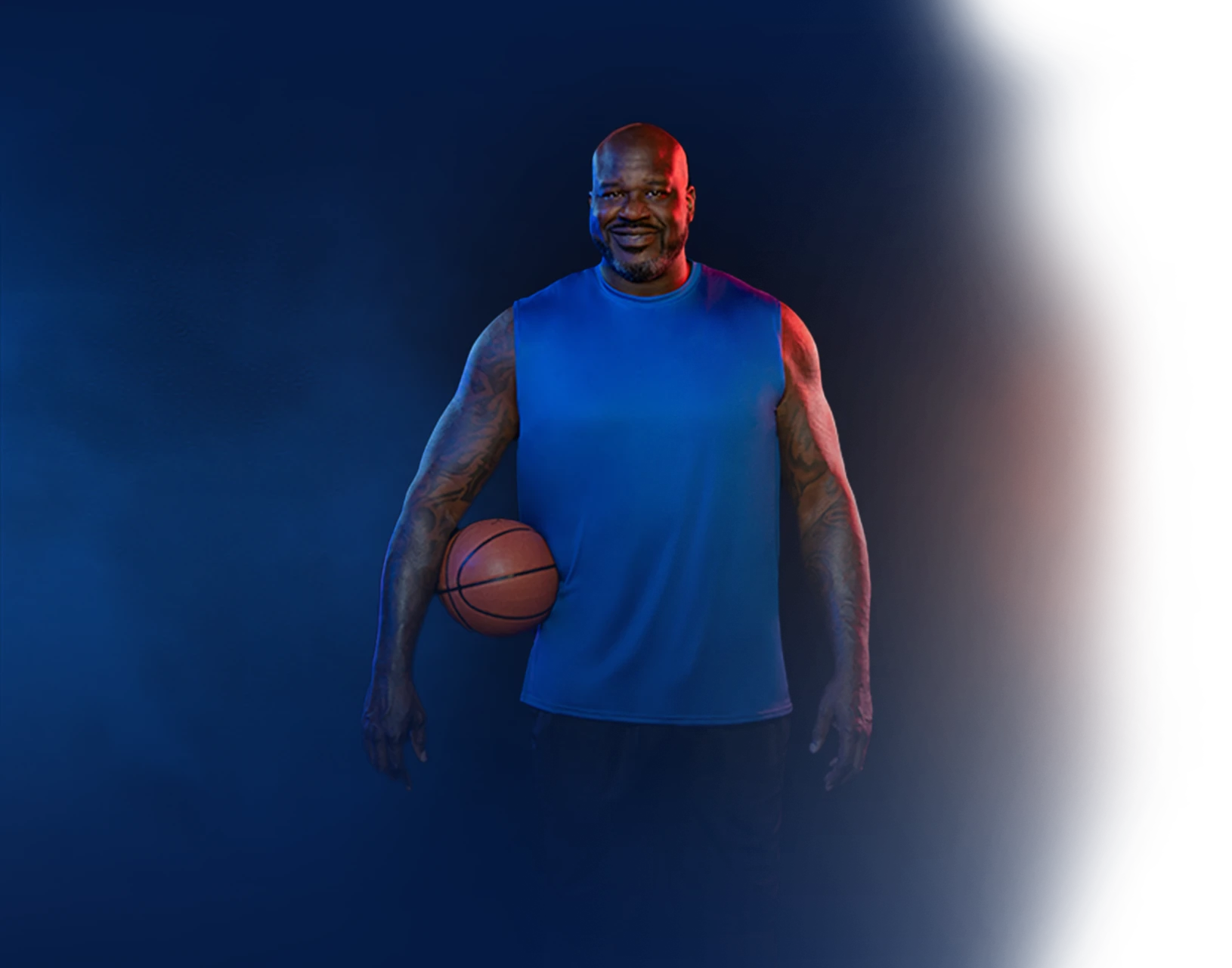 Shaquille O'Neil smiling as he holds a basket ball under his right arm.